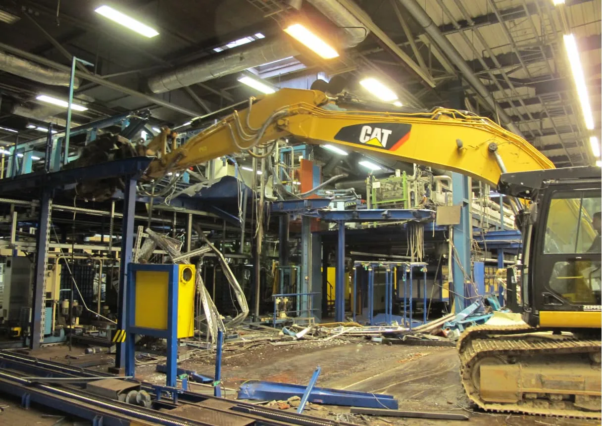 Abbruchbagger demontiert Maschinenanlage in einer Industriehalle
